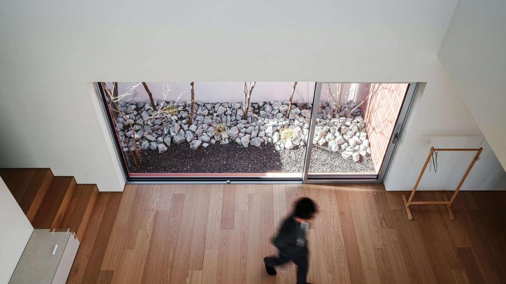 Unscharfe Person in einem hellen, modernen Wohnraum mit Holzfussboden und grosser Fensterfront.