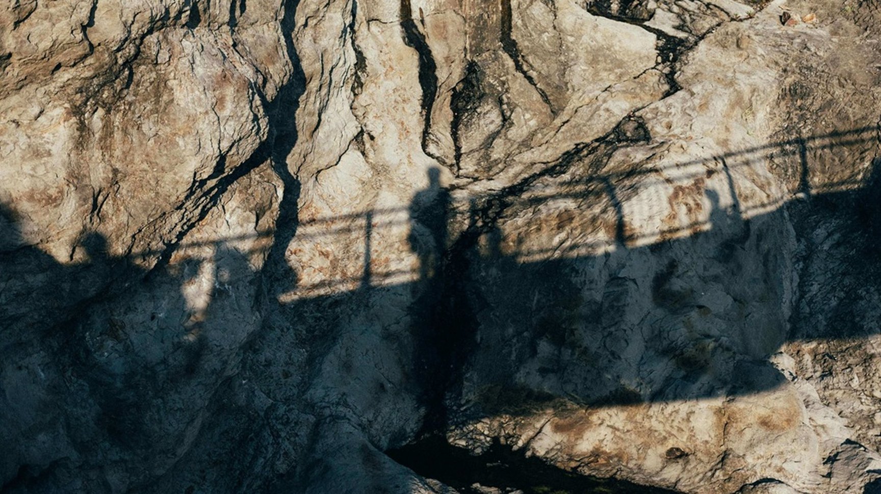 Schatten zweier Personen und einer Brückeauf einer sonnenbeschienenen Felswand